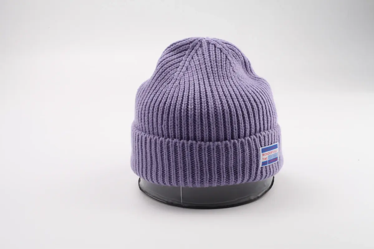 Purple rib-knit beanie with a folded cuff and small sewn label on a display stand