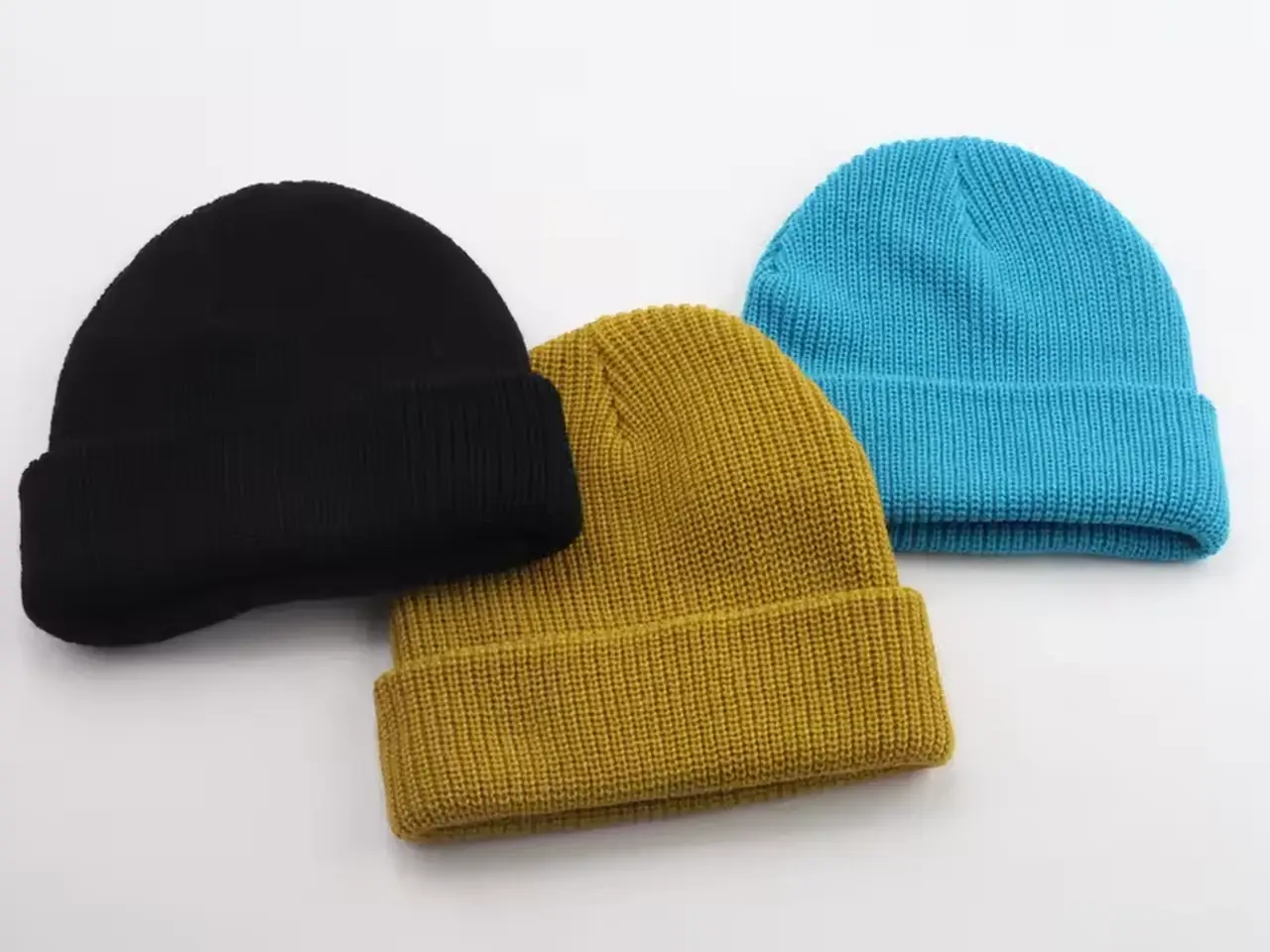 Three rib-knit beanies in black, mustard and blue arranged together