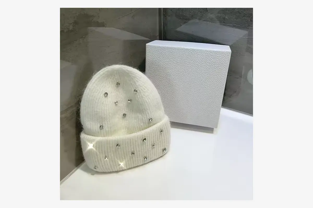 White knit beanie displayed beside a plain presentation box.