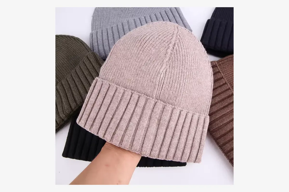 Hand holding a pink cuffed beanie beside other color samples.