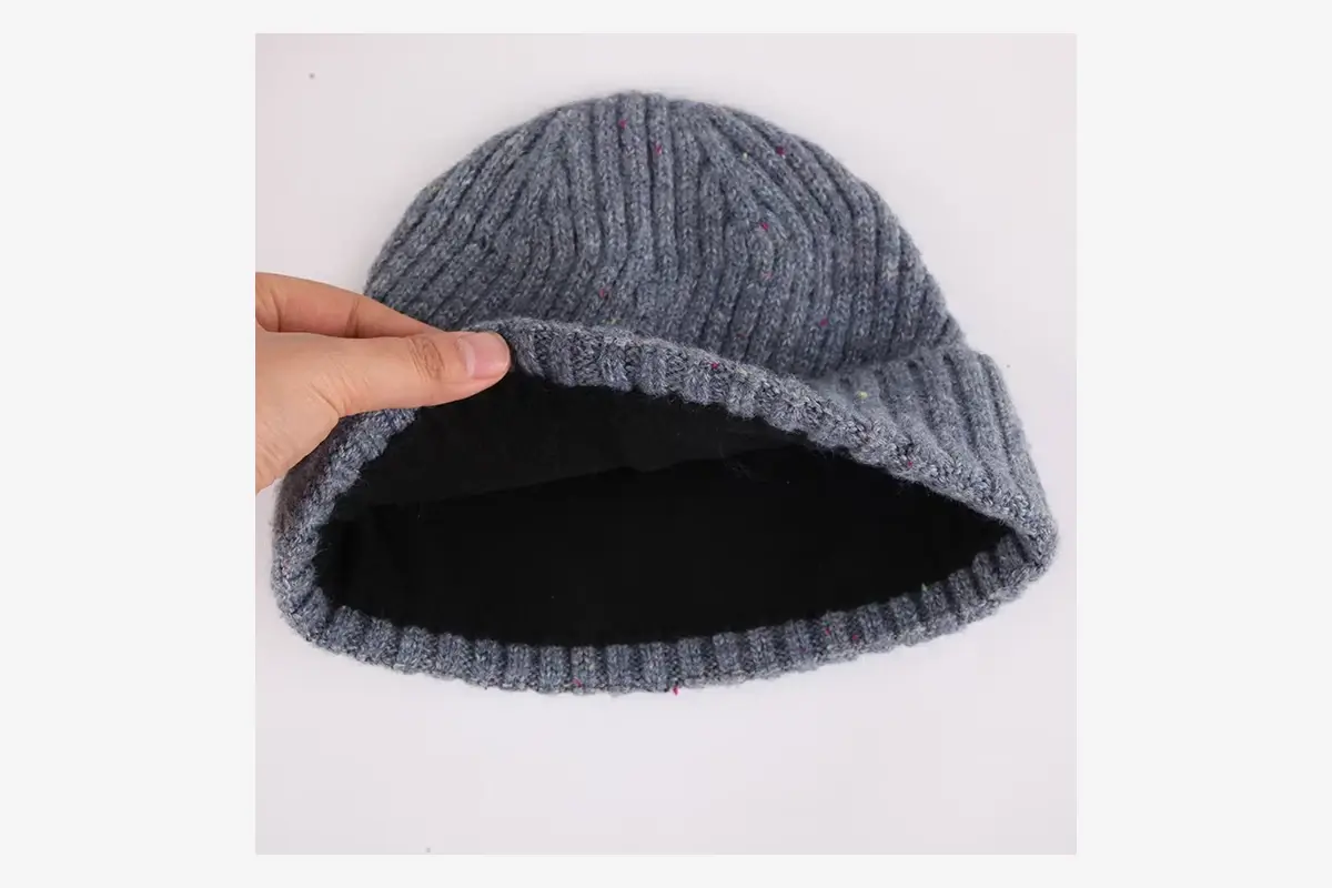 Hand lifting a gray knit beanie to show its black inner lining.