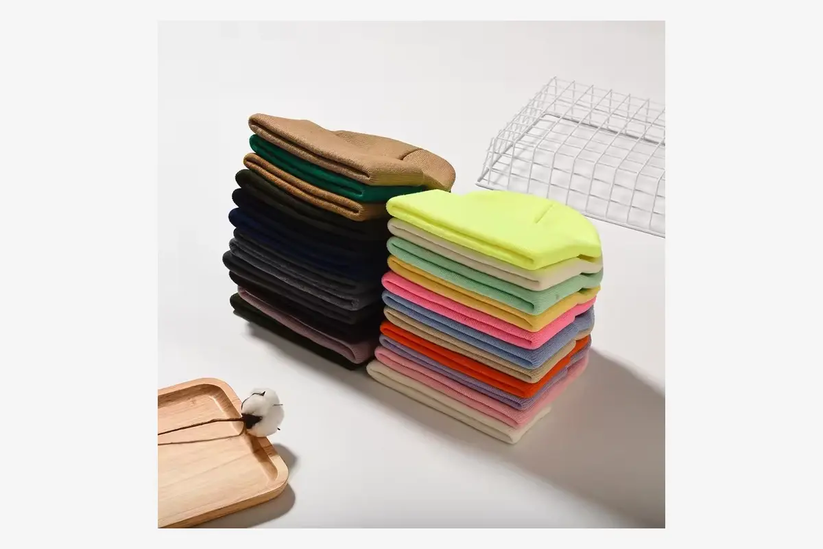 Stacks of finished knit beanies in several colors for sample comparison.