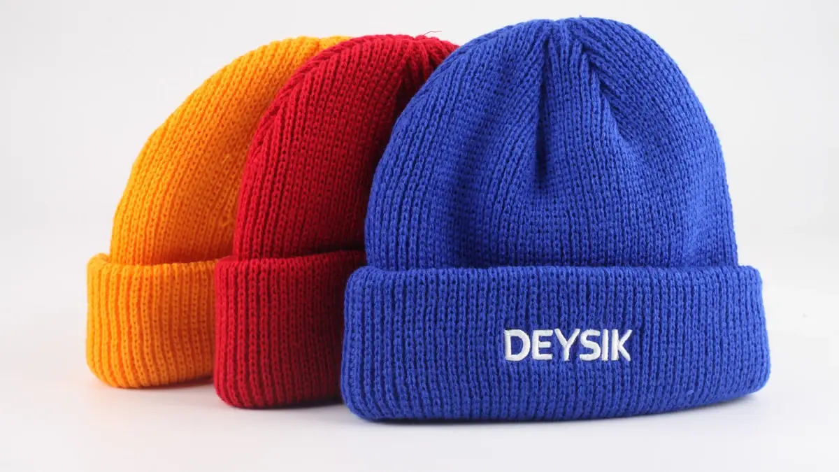 Three cuffed beanies in yellow, red and blue, with white lettering centered on the blue cuff.