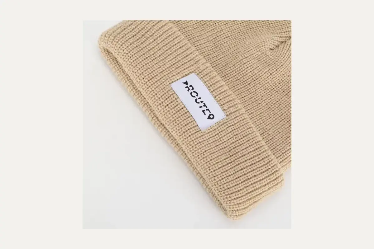 Close view of a sewn label on a beige knit beanie.