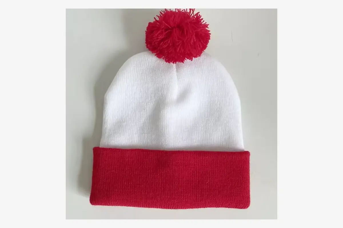 White knit beanie with a red cuff and red yarn pom pom.