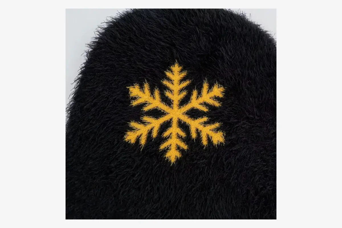 Close view of a yellow snowflake motif on a black fuzzy beanie.