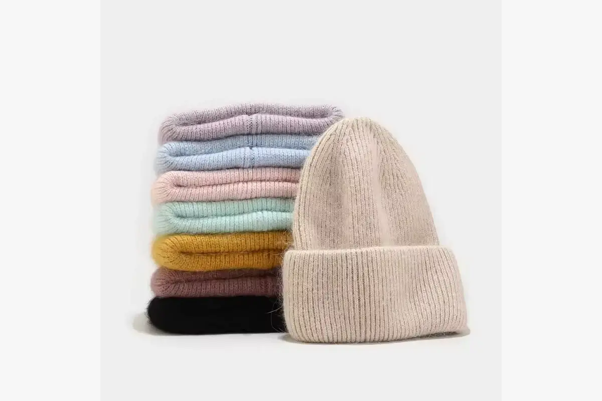 Cream cuffed beanie beside a stack of knit color options