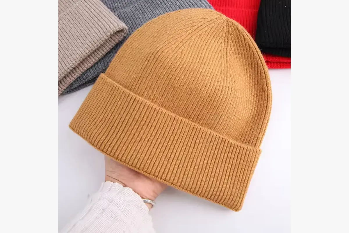 Hand holding a tan rib-knit beanie to show its folded cuff and texture