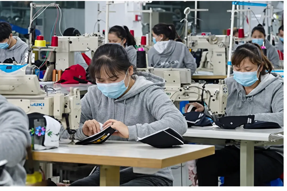 Factory workers checking headwear at sewing and production stations