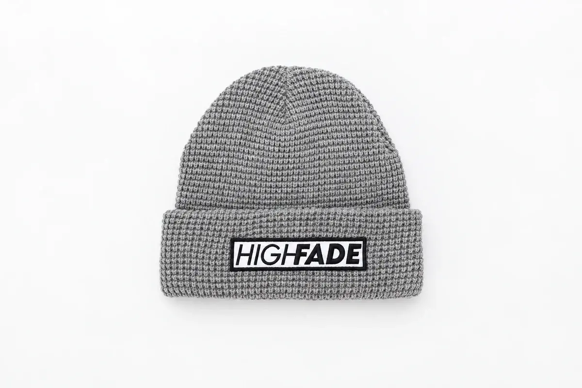 Gray ribbed cuffed beanie with a rectangular woven brand label centered on the folded cuff