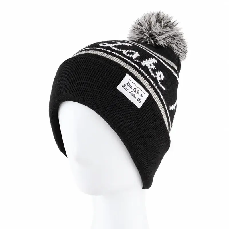 Charcoal beanie with a pale faux-fur pom and cuff label