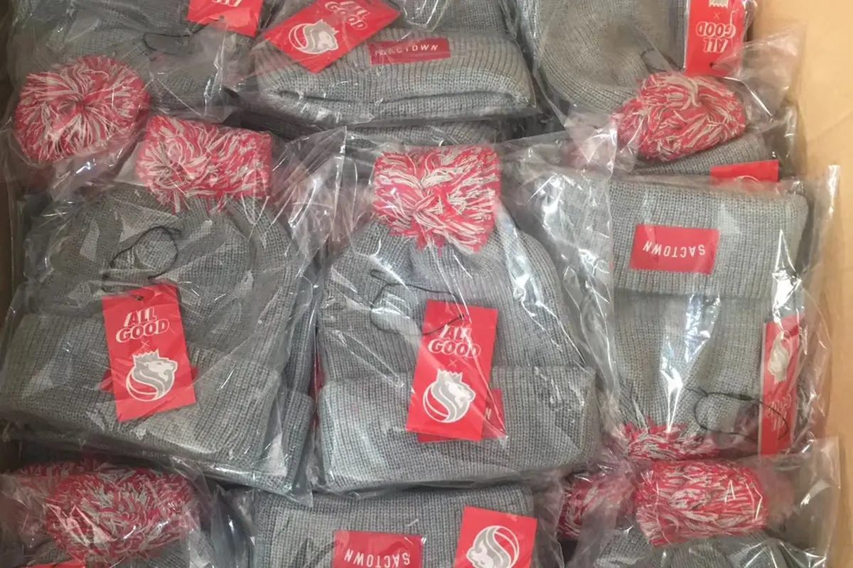 Individually bagged gray pom-pom beanies with red hangtags packed in a carton