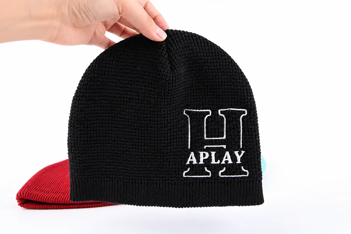 Hand holding a black rib-knit beanie with embroidered logo