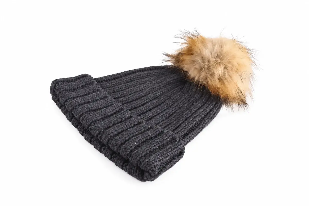 Side view of a charcoal cable-knit beanie with a relaxed crown and faux-fur pom