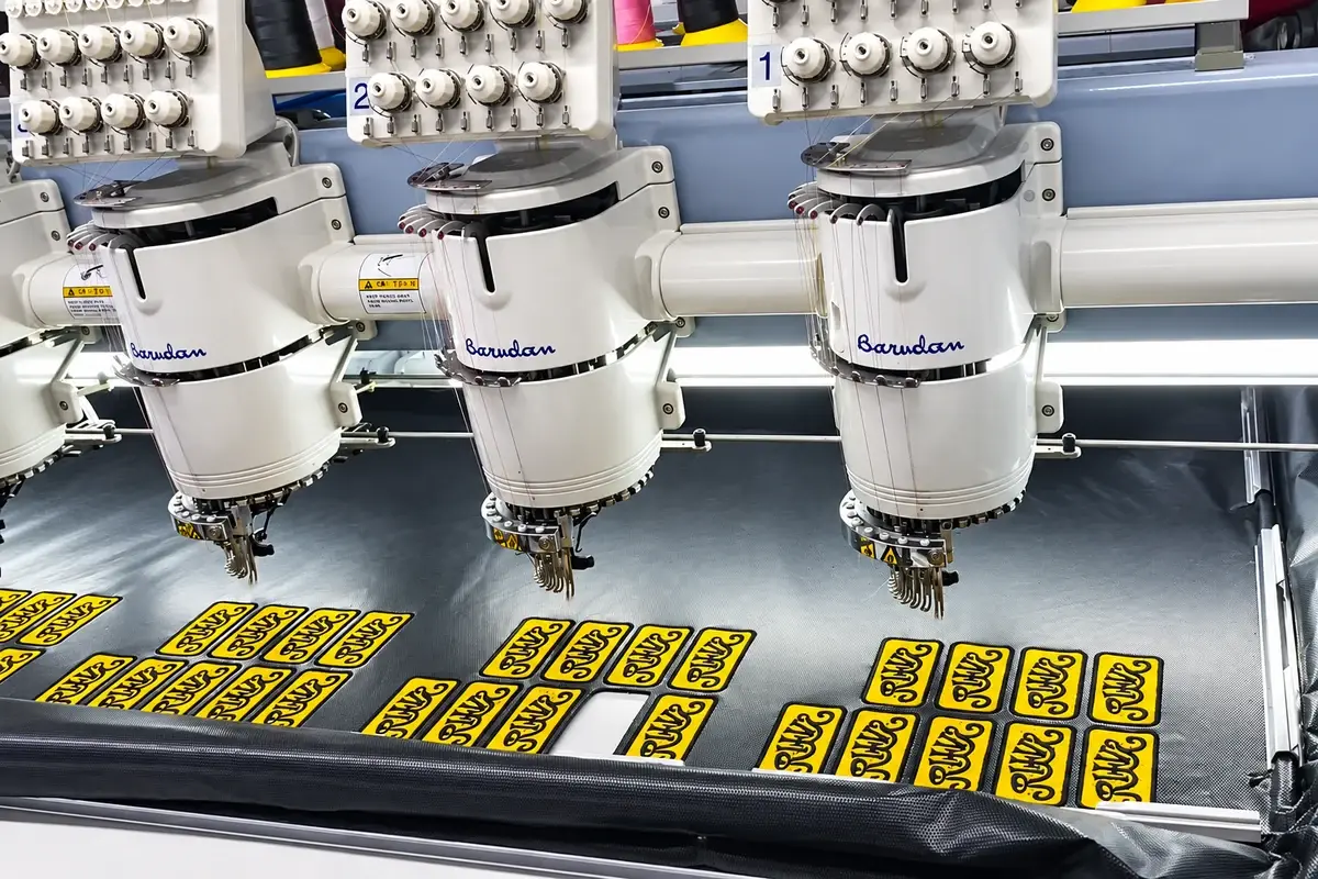 Three industrial knit embroidery machines producing yellow and black logo patches