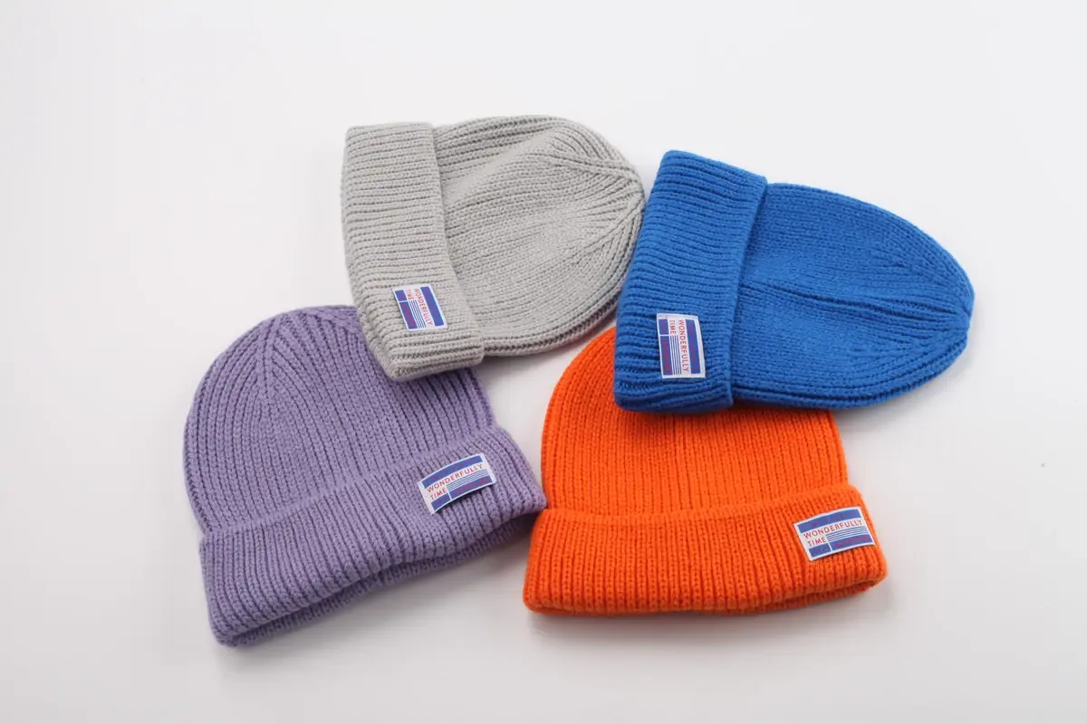 Four cuffed rib-knit beanies with small sewn front labels in lavender, gray, blue and orange