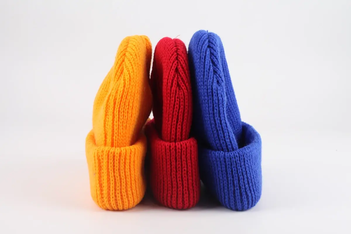 Four rib-knit beanies shown upright in orange, red, blue and charcoal