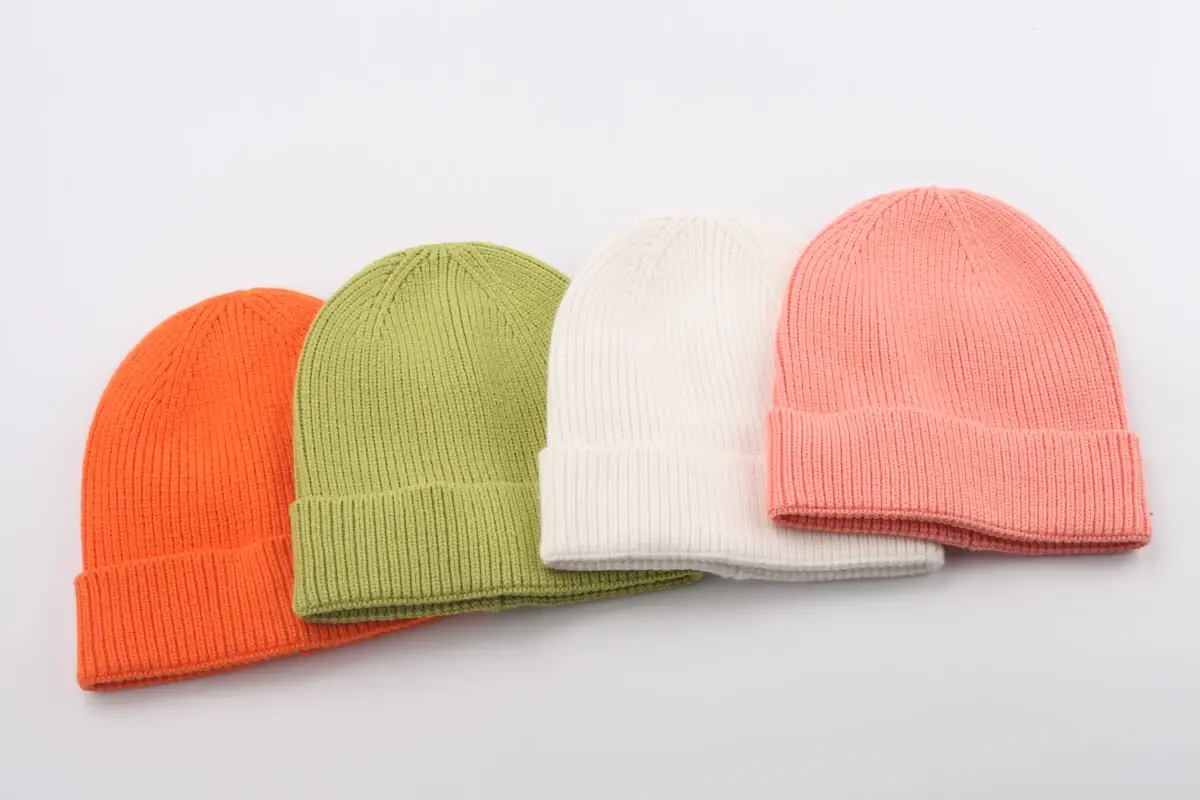 Four knit beanies in orange, green, white and pink