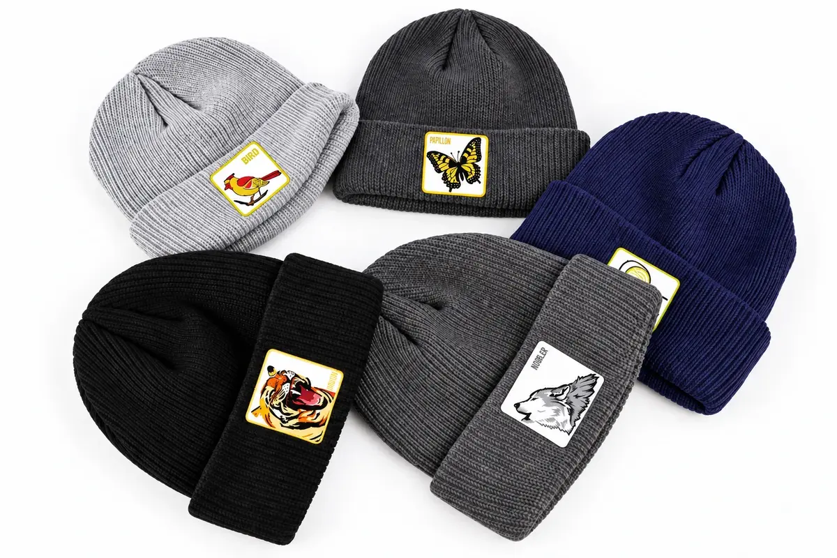 Six short knit beanies in gray, black, navy and white with folded cuffs and patches.