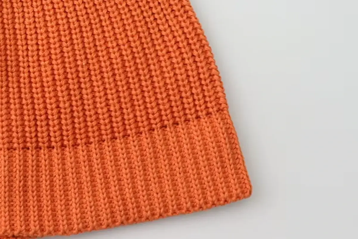 Close view of orange beanie stitches and the knitted lower edge