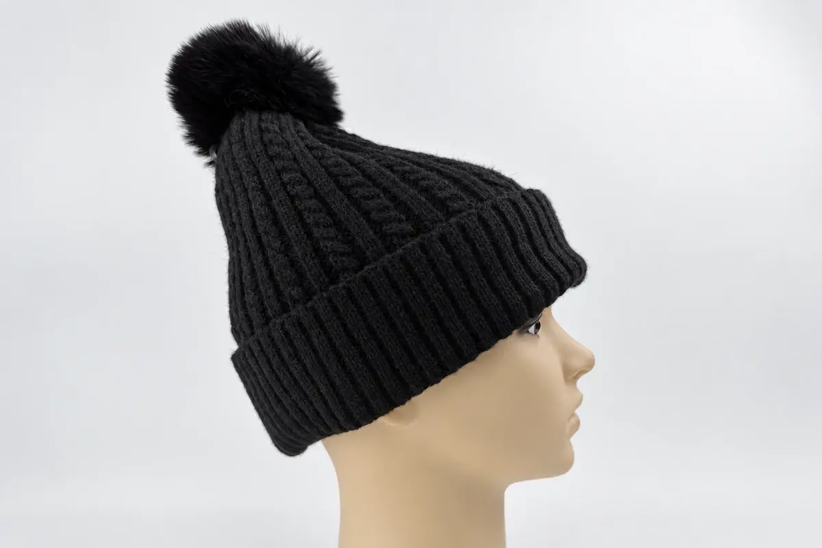 Side view of a long relaxed dark knit beanie with pom on a mannequin