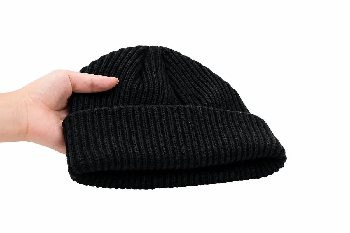 Side view of a short black rib-knit cuffed beanie showing its low crown and folded cuff