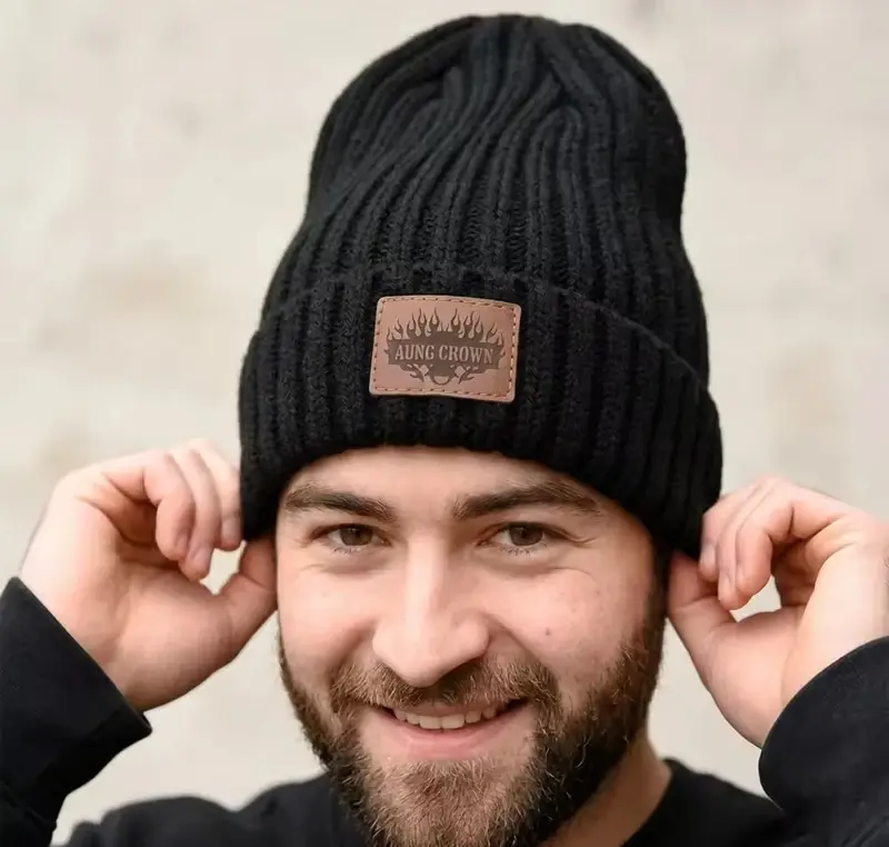 Black ribbed beanie worn by a man, showing a rectangular stitched cuff patch
