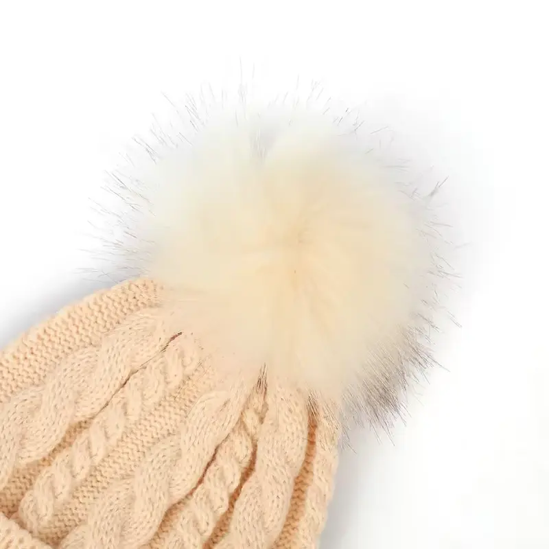 Close view of a pale pom pom attached to a cable-knit beanie