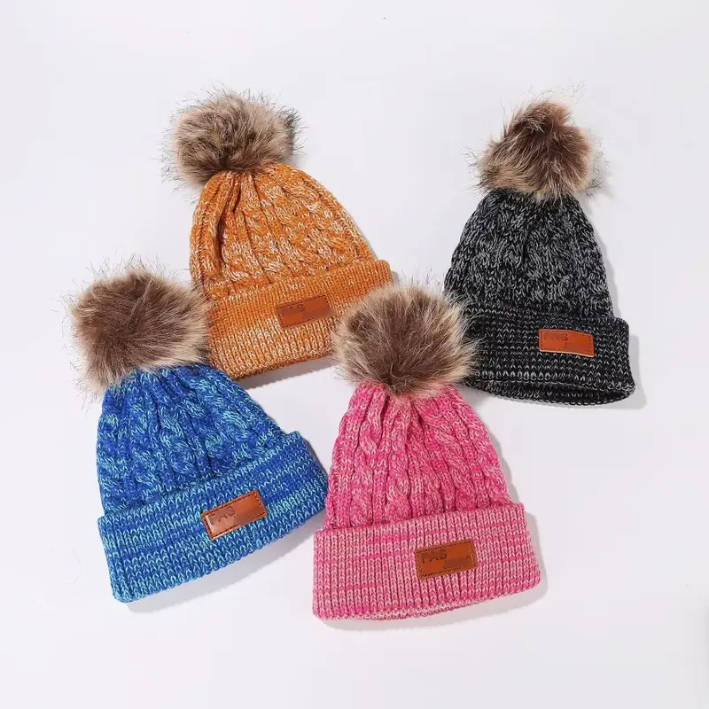 Four double pom beanies with branded patches on their folded cuffs