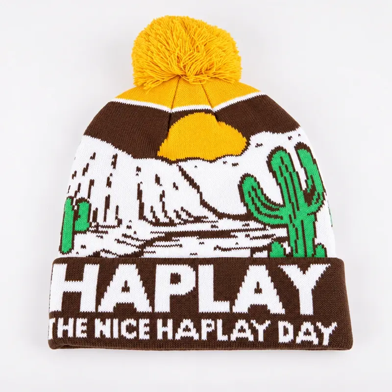 Yellow, brown and white holiday beanie with a large yarn pom and knit lettering