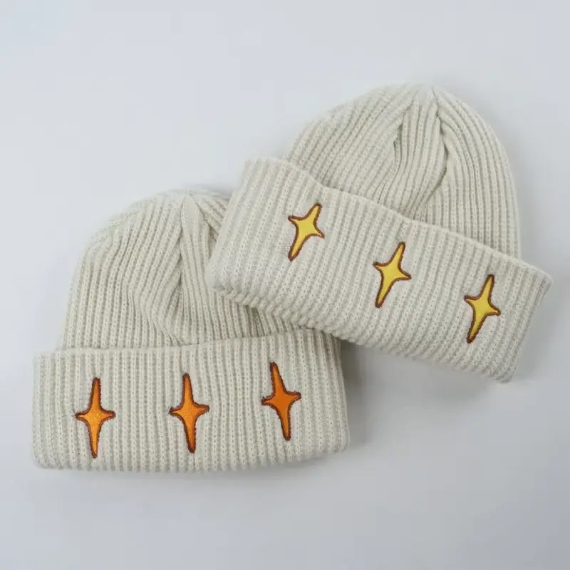 Cream rib-knit beanies with gold star embroidery on their folded cuffs