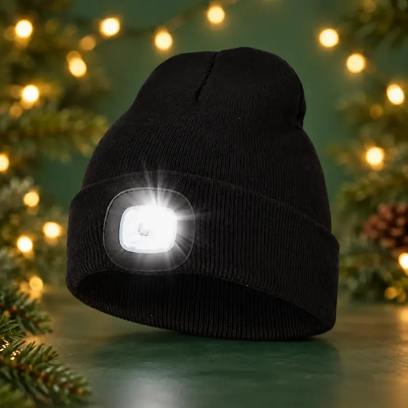 Black knit LED beanie with its front lamp lit against festive lights