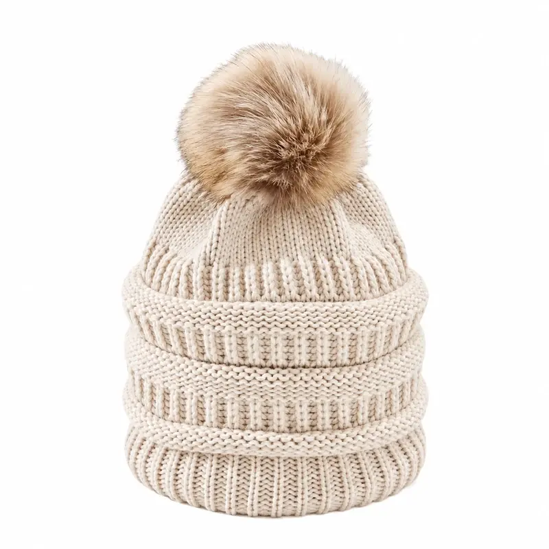 Cream cable-knit beanie with a tan faux fur pom, shown from the front