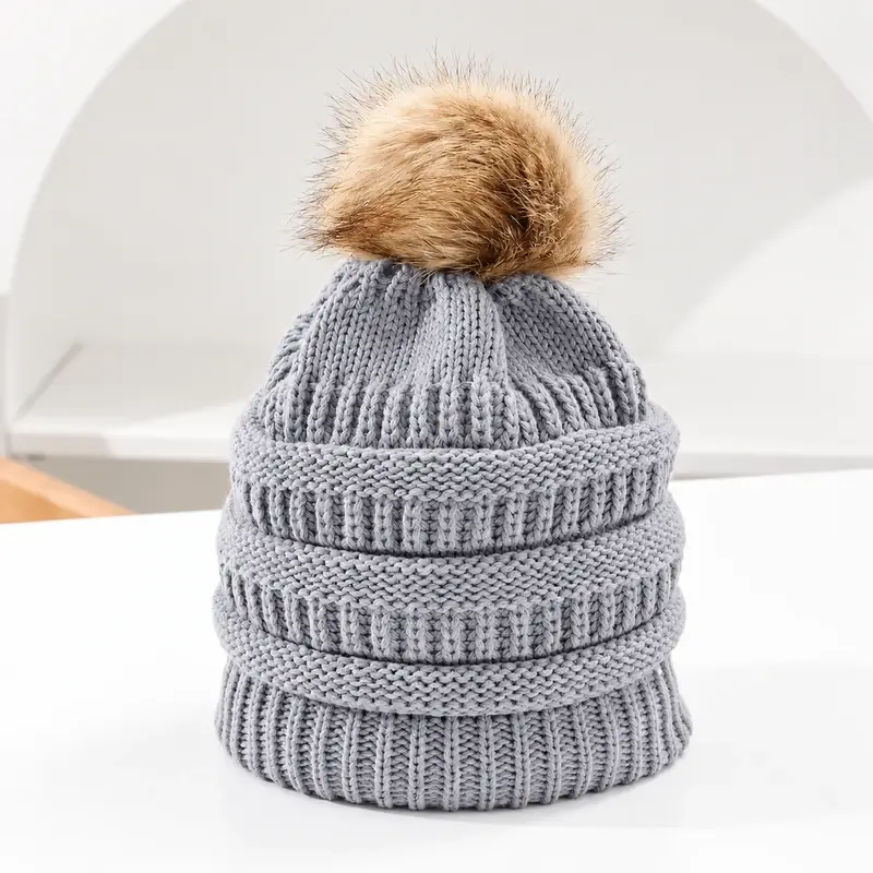 Light gray cable-knit beanie with a tan faux fur pom, front view