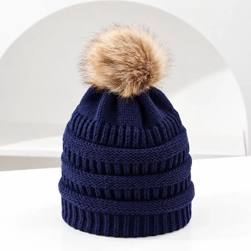 Navy cable-knit beanie with tan faux fur pom, front view
