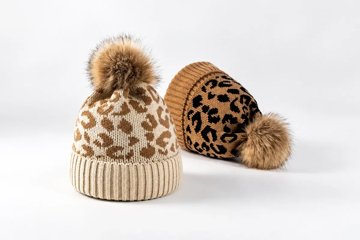 Two knit beanies with patterned shells and faux fur poms