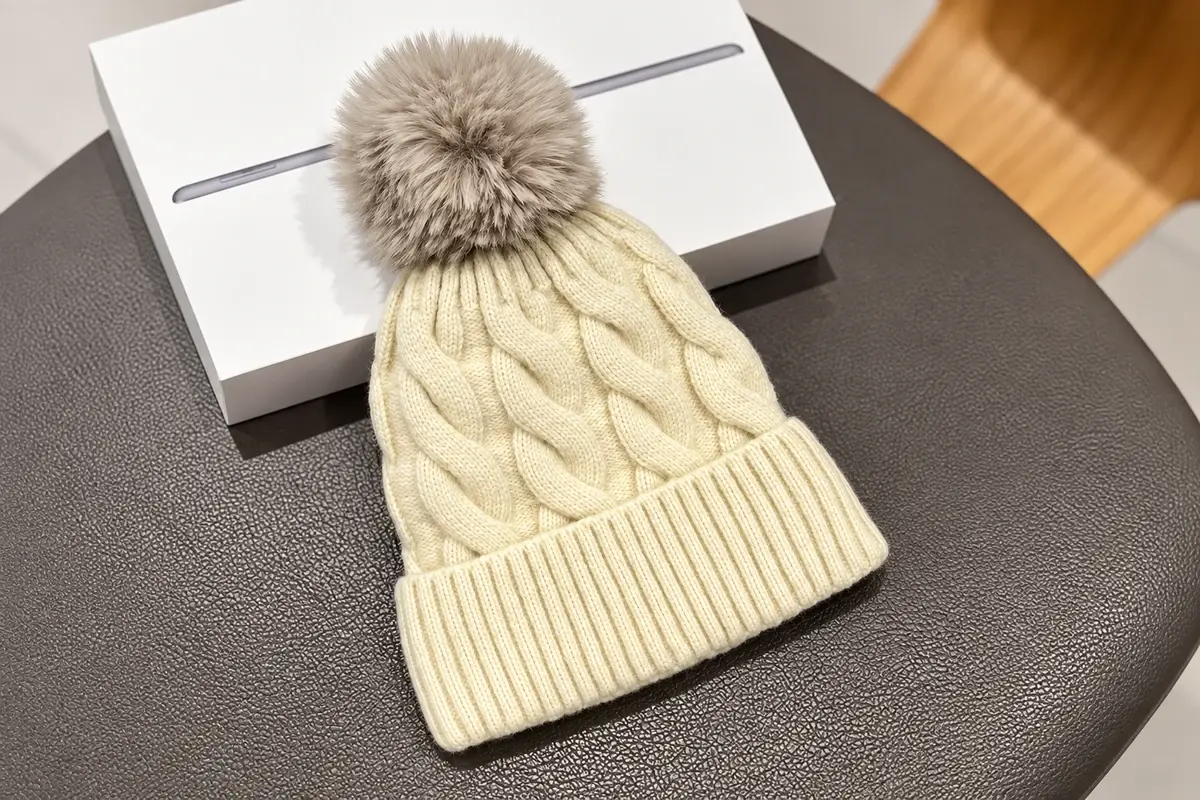 Cream cable-knit beanie with folded cuff and gray faux fur pom