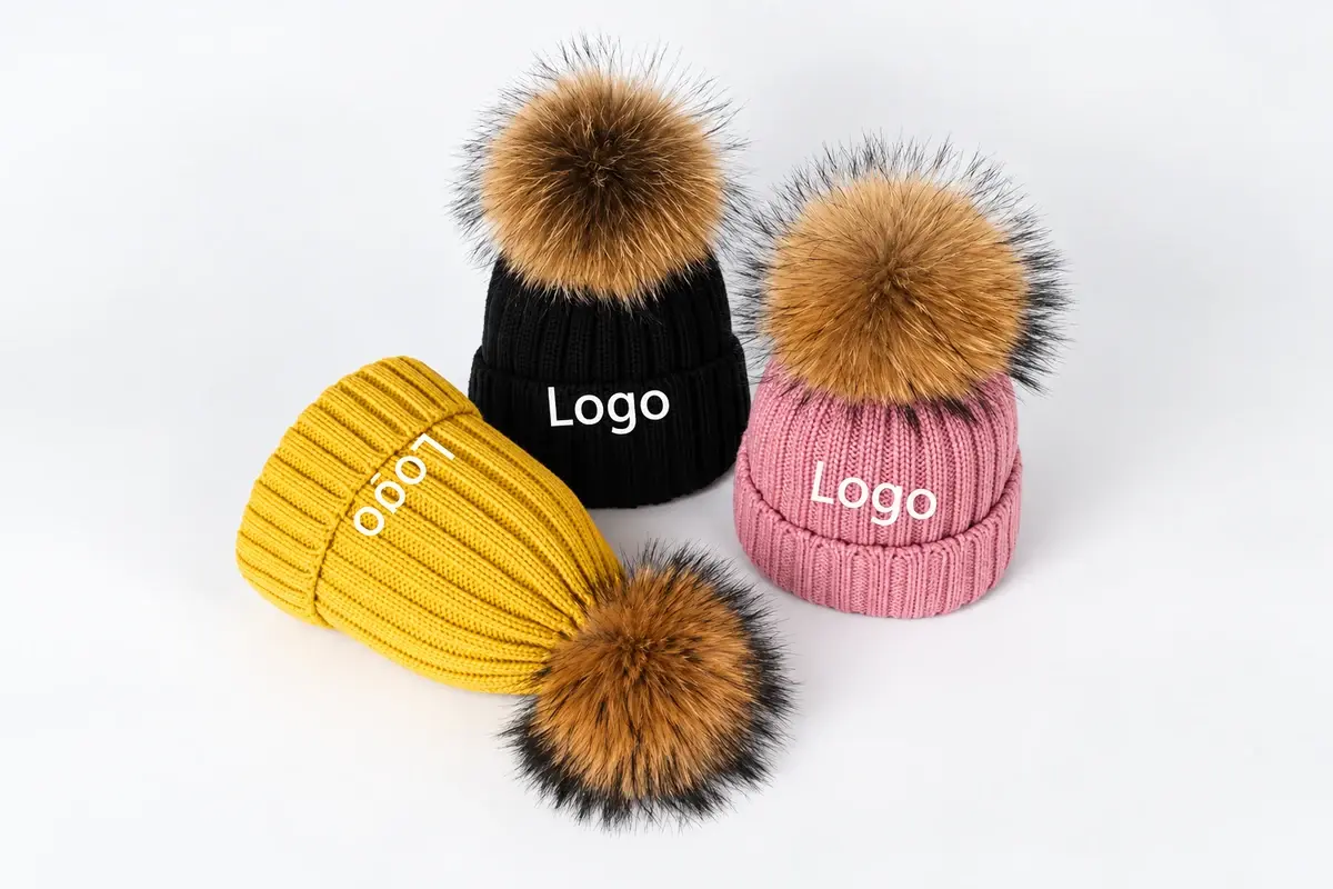 Two branded beanies with faux fur poms and visible cuff logos
