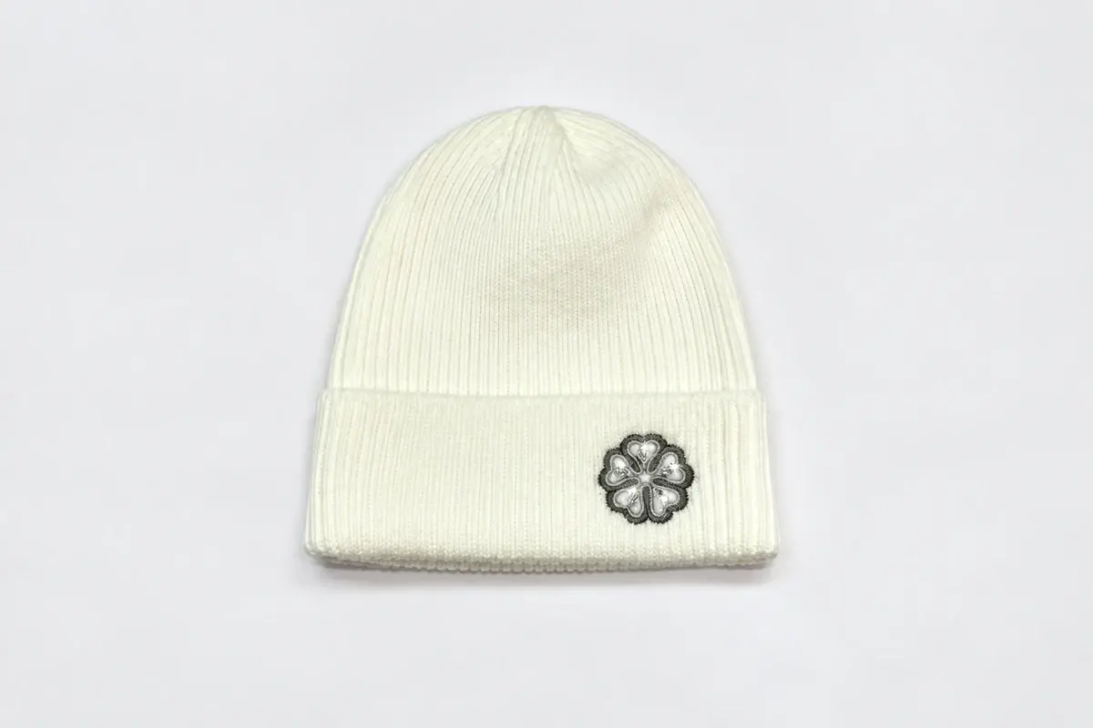 Cream rib-knit cuffed beanie with a small embroidered flower emblem on the cuff