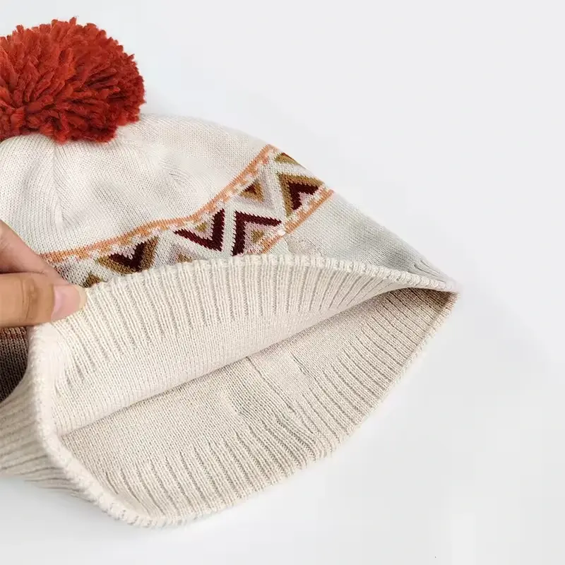 White knit beanie with a red pom and a geometric jacquard band