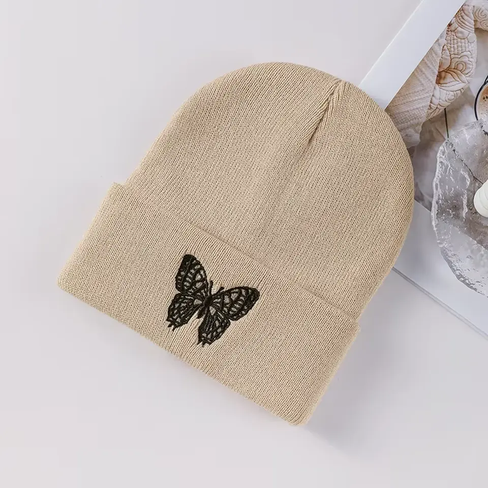 Beige cuffed beanie with a black embroidered butterfly on the cuff