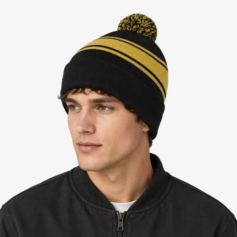 Side view of a black and yellow striped pom pom beanie worn on a model