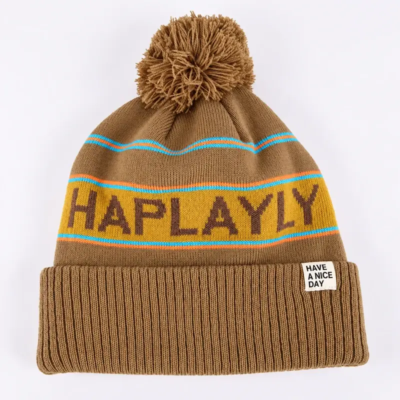 Tan jacquard pom pom beanie with turquoise and orange stripes and HAPLAY lettering