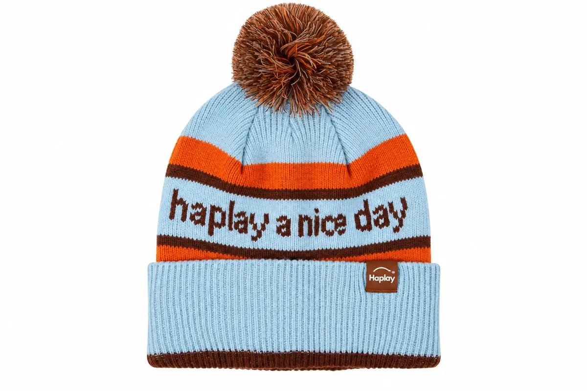 Pale blue pom pom beanie with orange jacquard wording and Haplay woven label