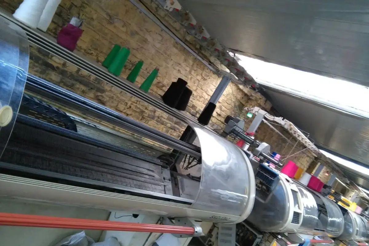 Close view of a flat knitting machine bed and yarn cones in a workshop