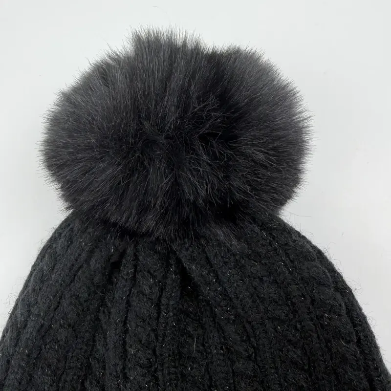 Close-up of dark knit stitches and fuzzy pom-pom fibers