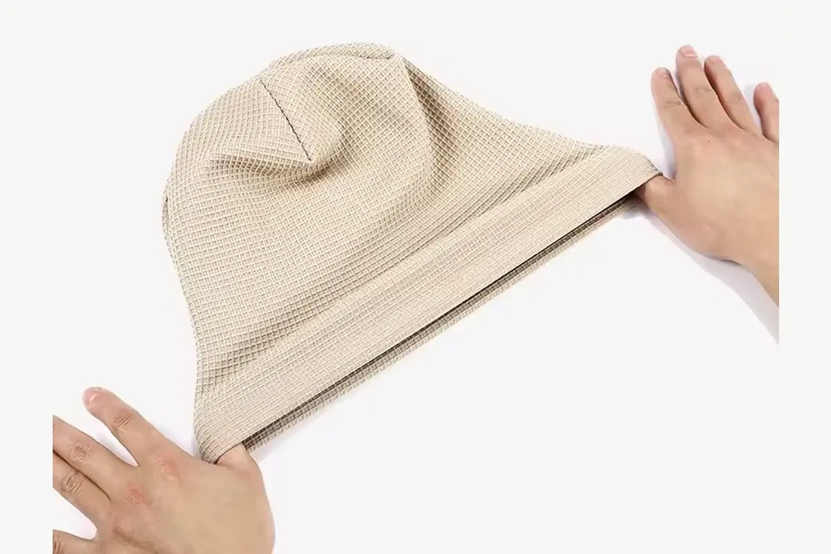 Hand stretching the edge of a beige slouchy knit beanie