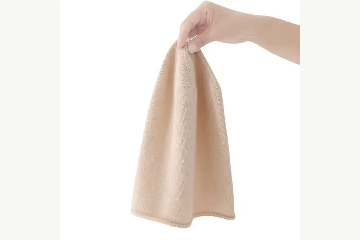 Hand holding a beige knit beanie to show its thin, flexible body
