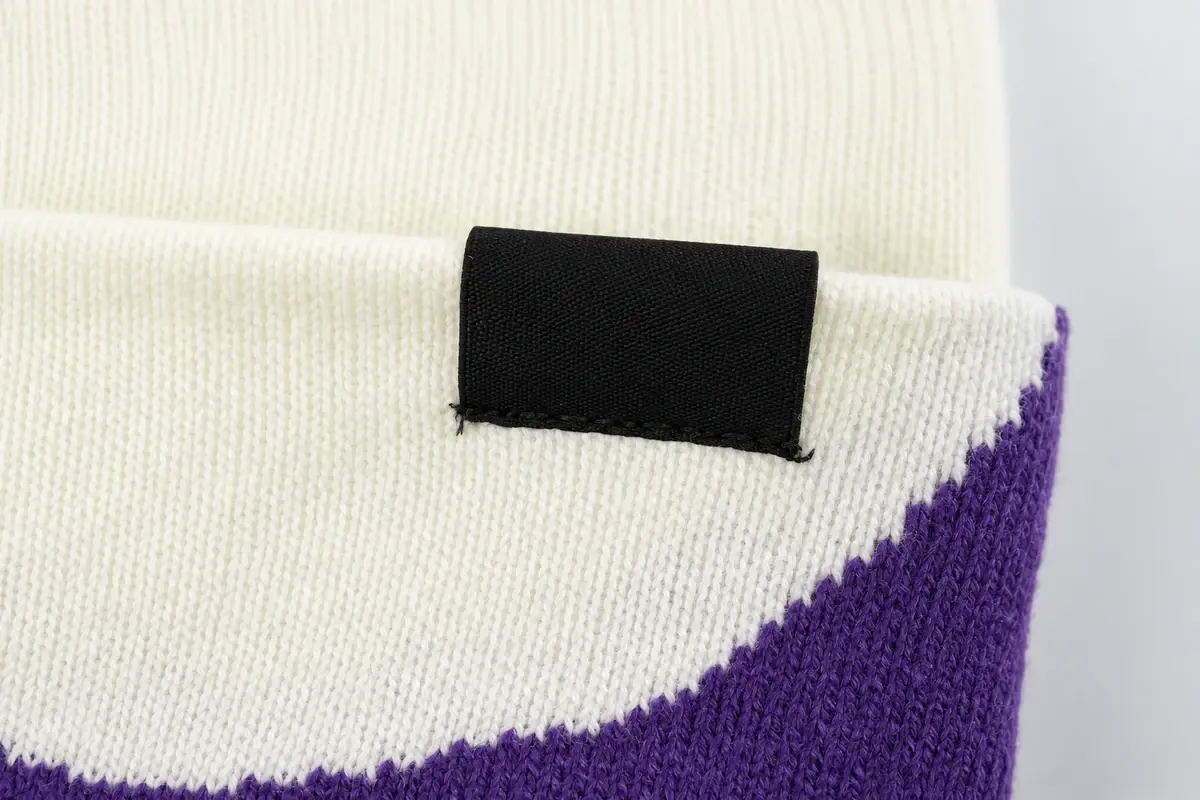 Blank black woven label sewn to a white and purple knit beanie