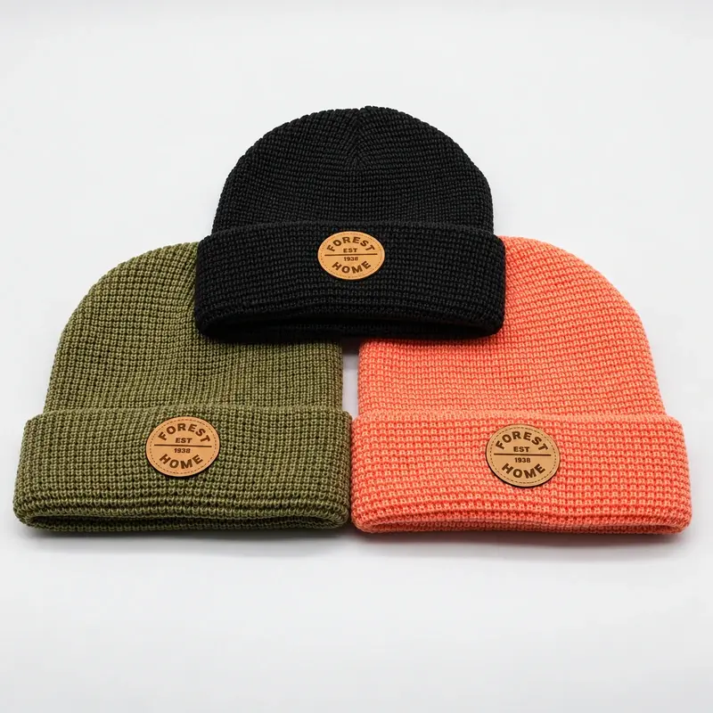 Three short fisherman beanies in olive, black, and coral with tan oval patches